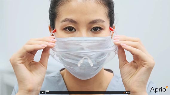 A person puts on a medical face mask with a clear nasal insert, holding the mask by its ear loops.