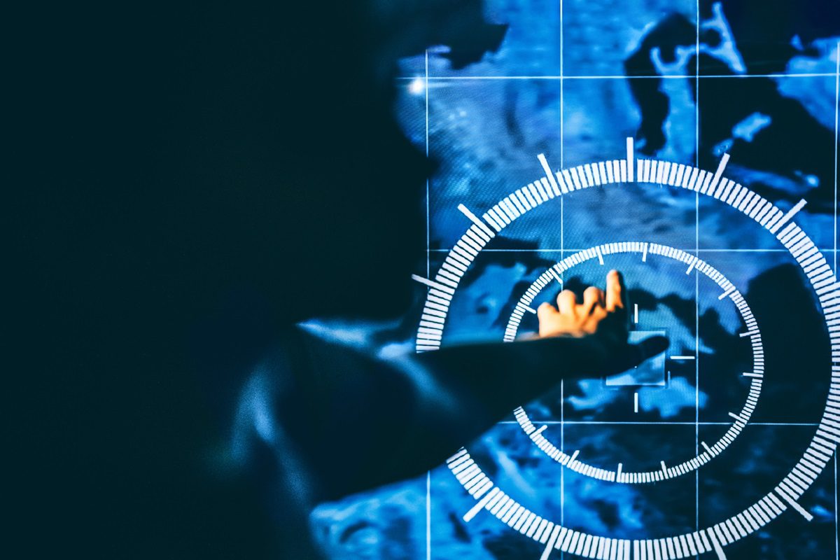 A hand reaches toward a digital screen displaying a blue map with concentric circular graphics and white grid lines, suggesting interaction with futuristic or virtual technology—an image that resonates with contractors navigating systems or awaiting updates as CMMC Phase 2 remains on hold.