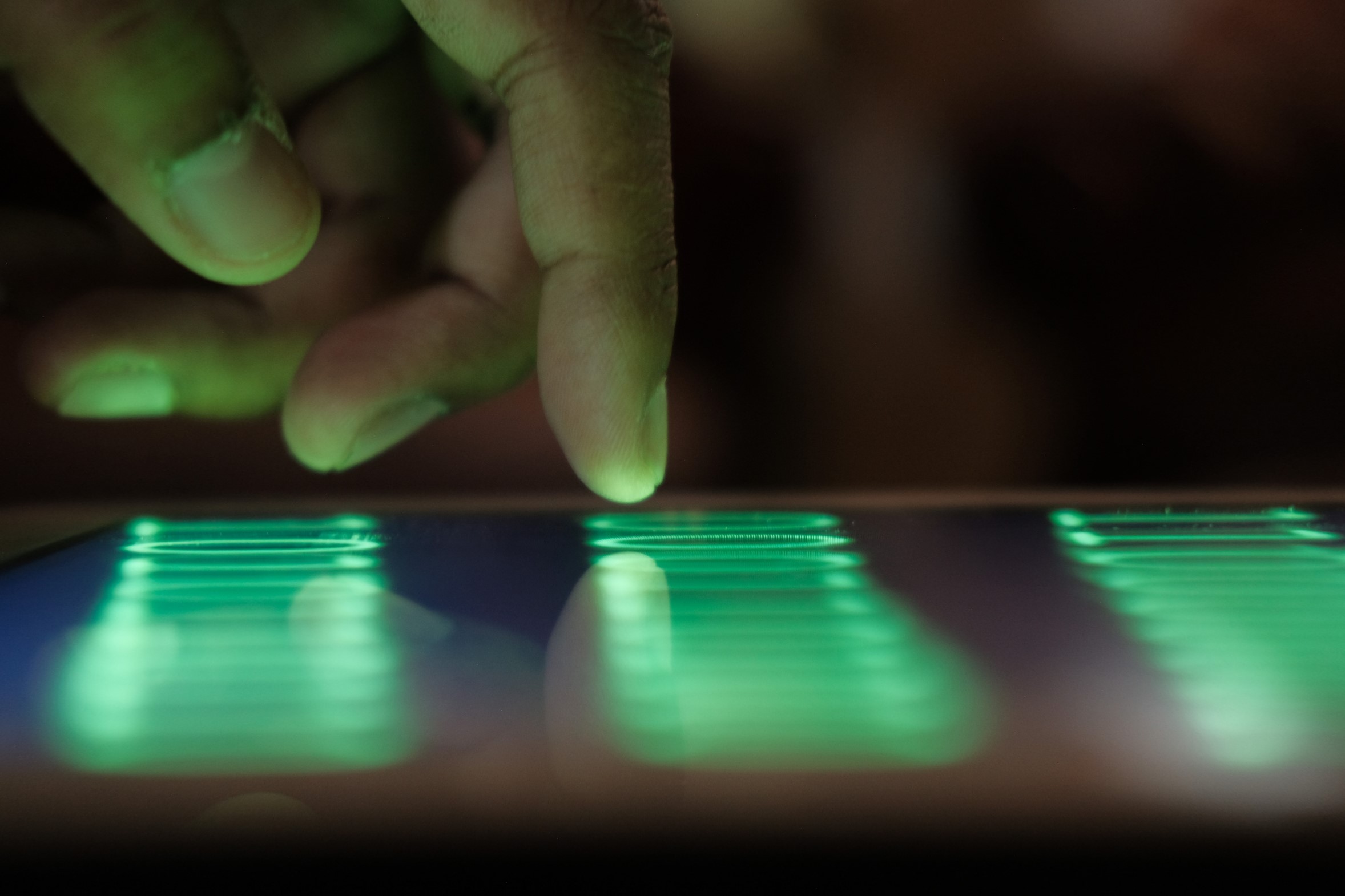 A close-up of a persons fingers touching a digital screen displaying glowing green lines, suggesting interaction with a touchscreen device.